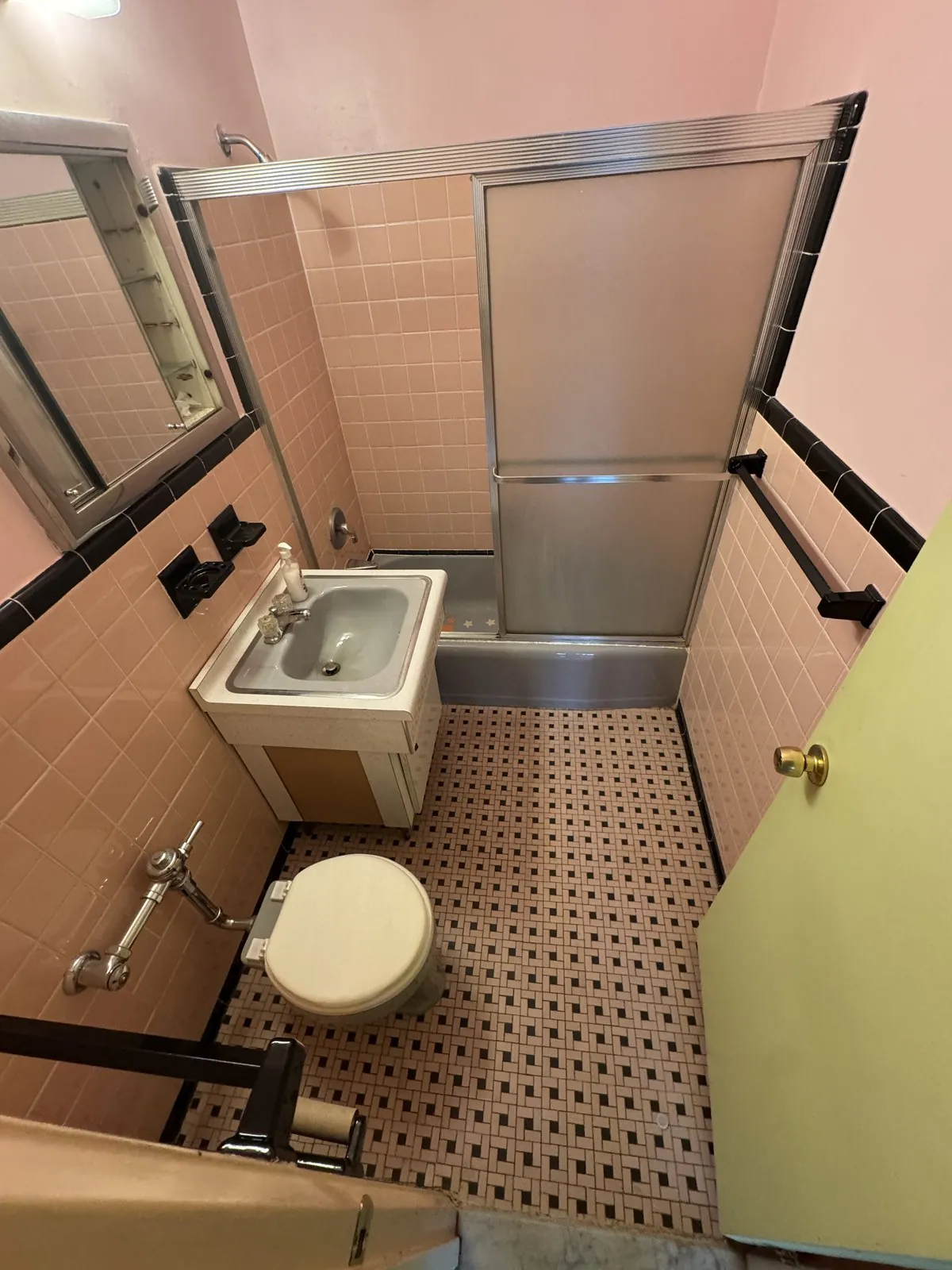 Dated peach-tile bathroom with a tub, wall sink and toilet before the renovation