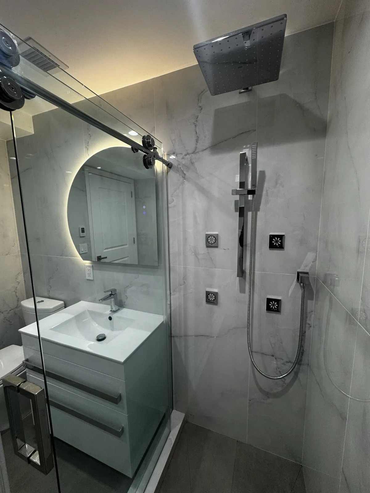 Marble walk-in shower with rain head, hand shower and body jets behind frameless glass