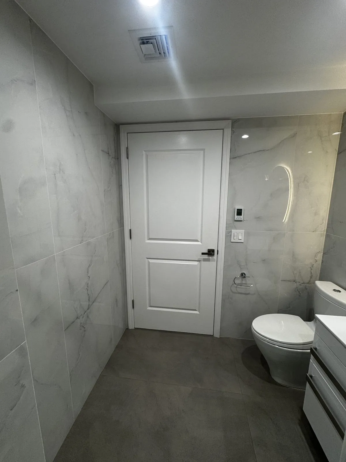 Wide view of the finished marble bathroom toward the door, with wall-hung toilet