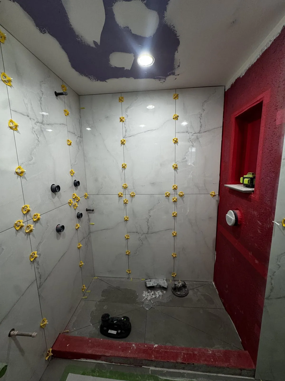 Large-format gray marble going up over the red waterproofing, with leveling clips