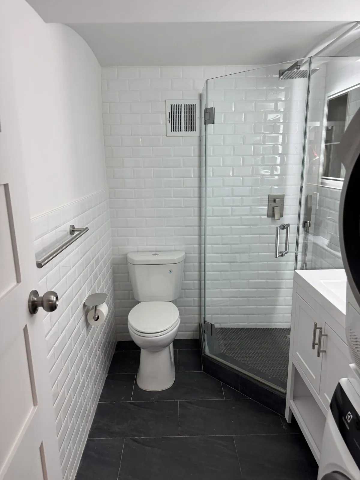 Finished subway-tile bathroom with glass shower and stacked washer-dryer