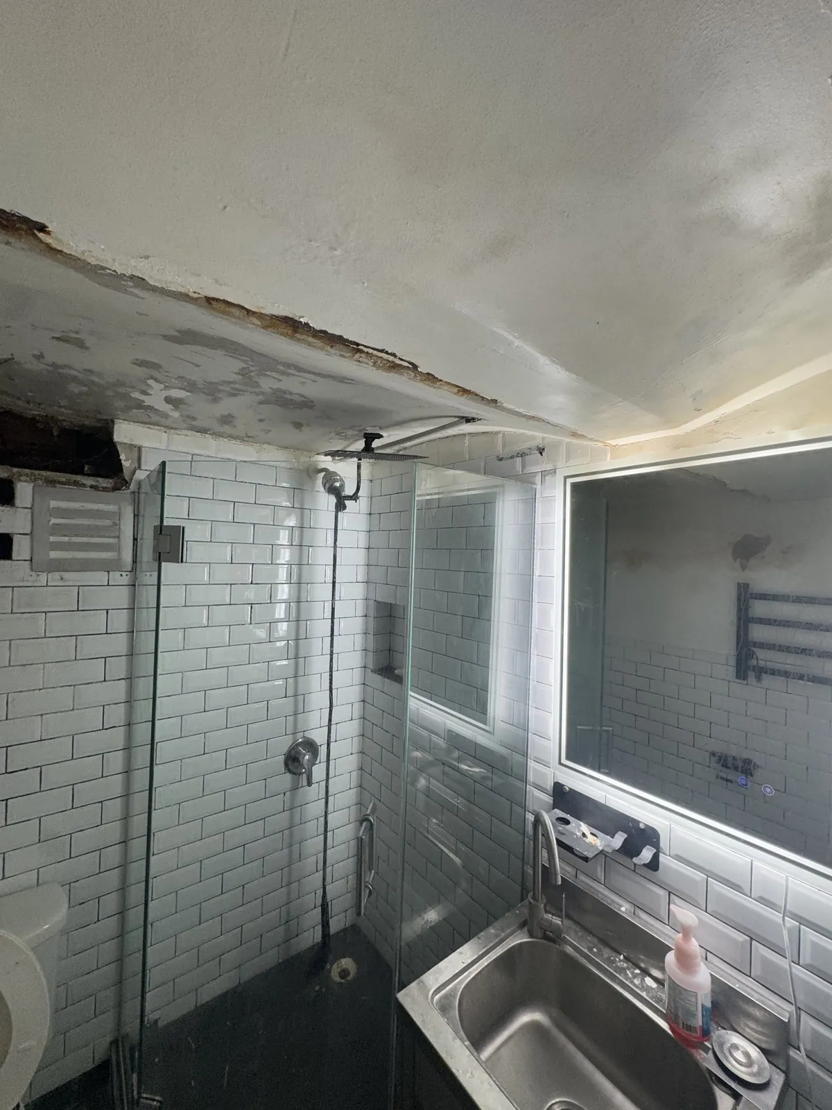 Water-soaked ceiling peeling above the subway-tile shower