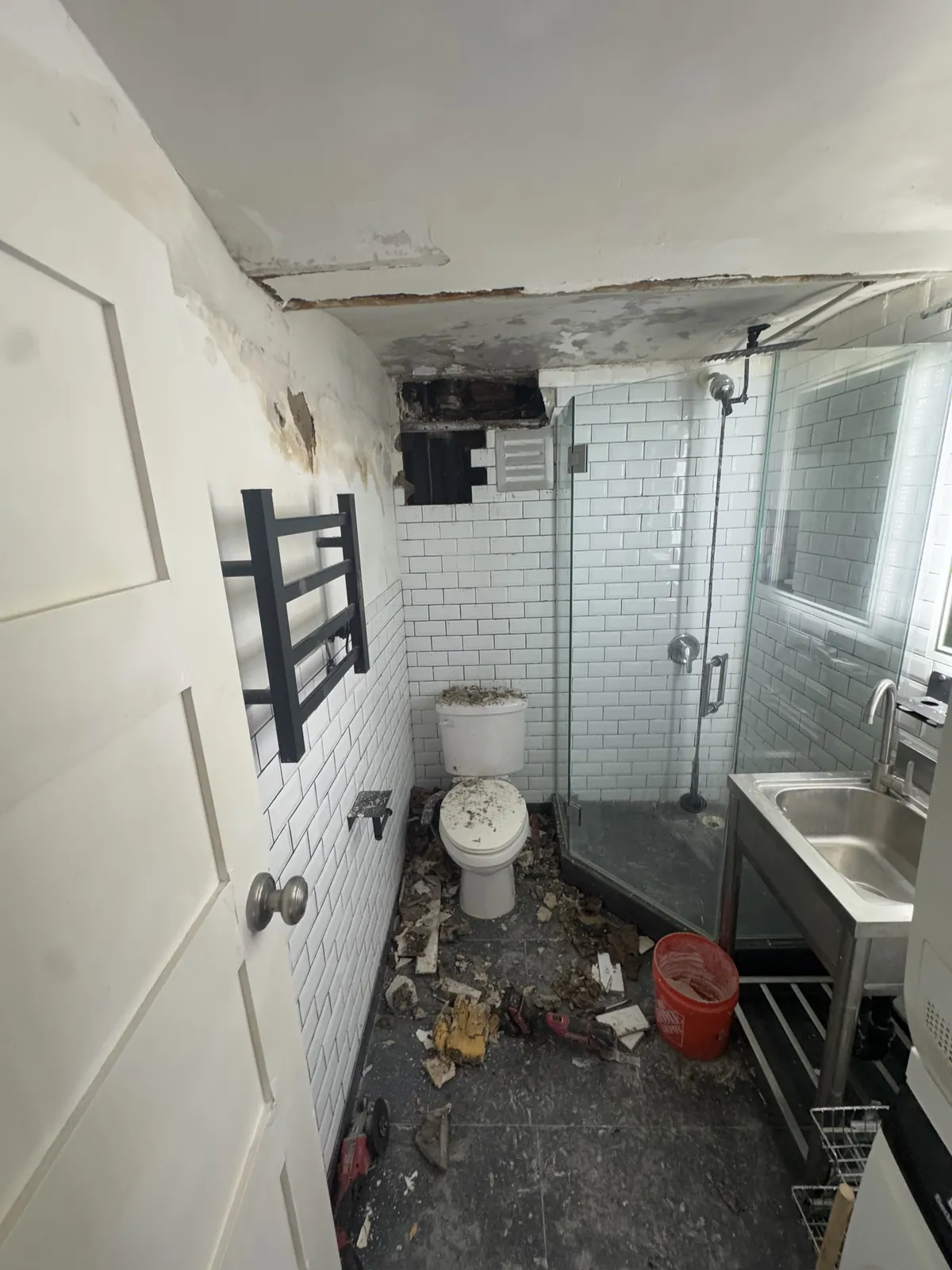 Flood-wrecked subway-tile bathroom, debris across the floor and a caved ceiling