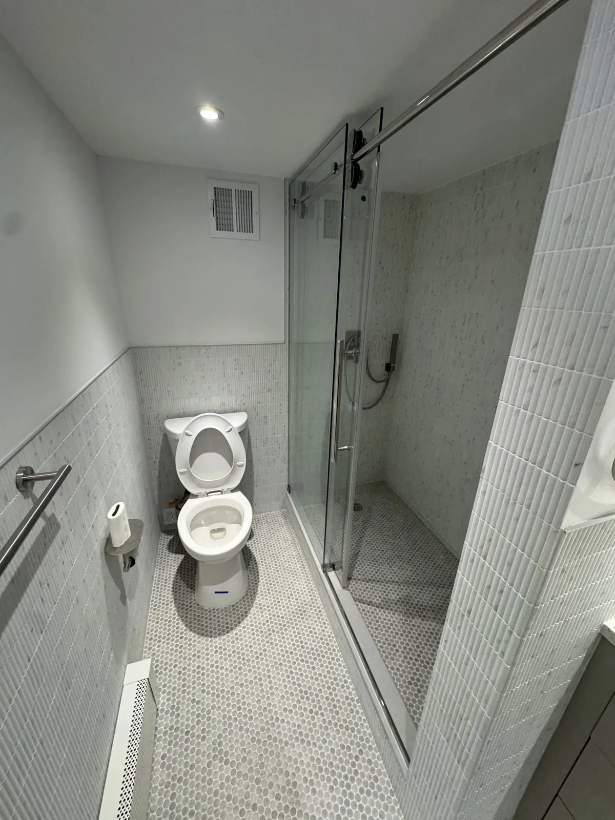 Second bathroom finished in white marble with a glass shower and penny-tile floor
