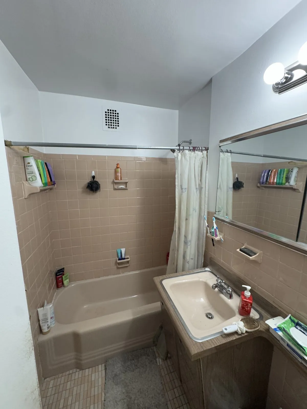 Original peach-tile tub with shower curtain and dated wall sink