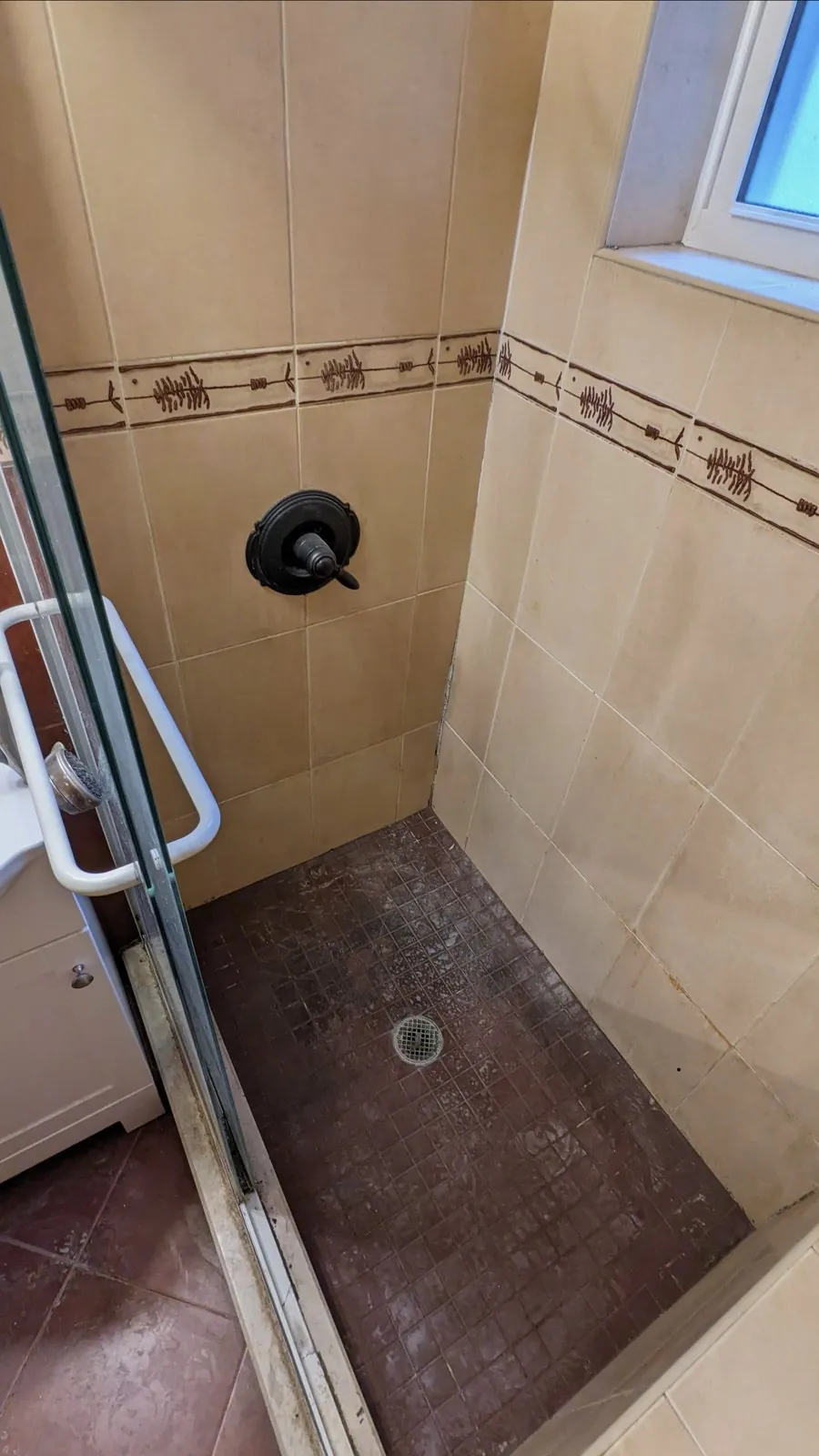 Dated almond-tile bathroom with a painted border and old framed sliding shower door