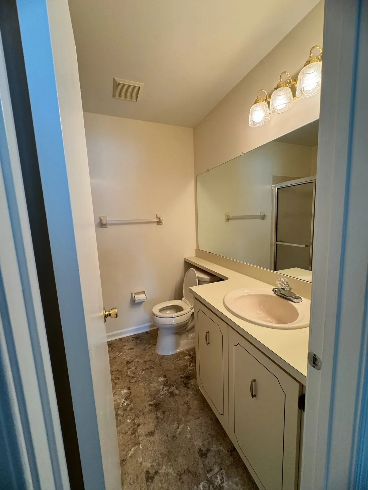 Dated bathroom with a cream laminate vanity, wall sink and toilet before the gut