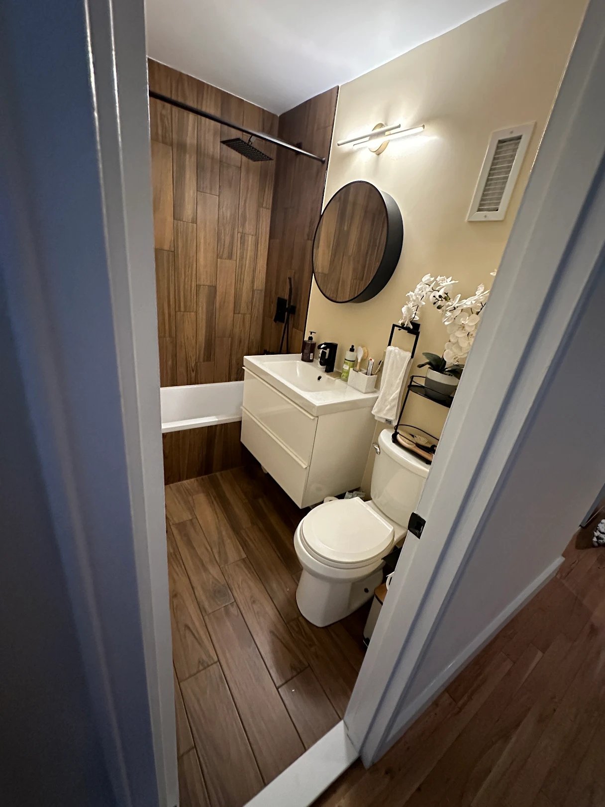 Walk-in shower retrofit with wood-look tile and round mirror